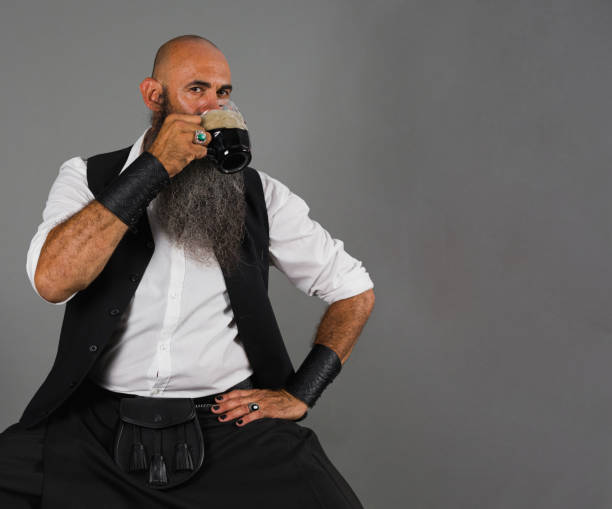 istock a mature man with his head shaved and long beard drinking a black beer while looking at camera ahead a gray background 1480347979