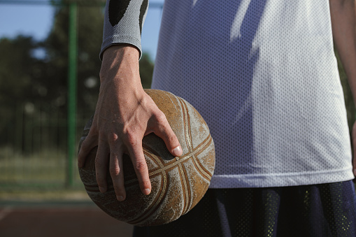 Crop male streetball player standing with ball in hand on summer basketball playground on sunny day