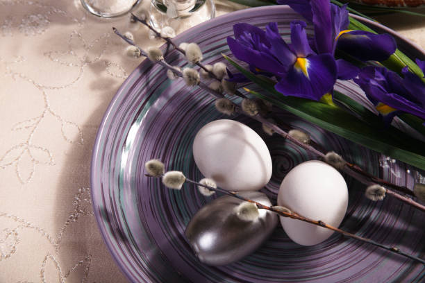 istock Easter table setting idea with violet iris flowers, willow branch and white and silver eggs on violet plate. 1480357472