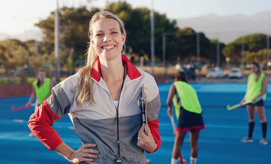 Hockey, coach and portrait of woman at stadium for training, fitness and cardio with group, happy and excited. Sports, trainer and female smile, confident and cheerful during game, match and sport