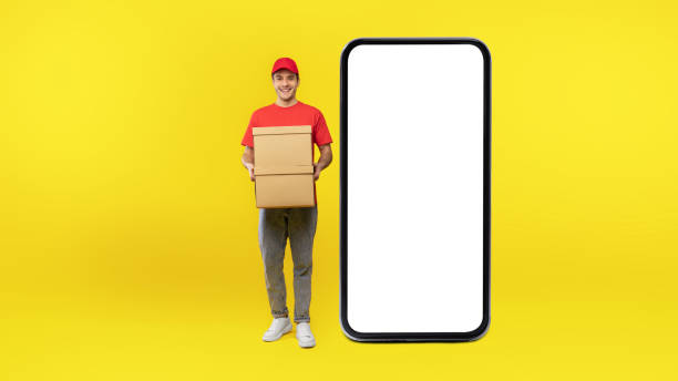 istock Courier Guy Posing Near Huge Cellphone Holding Boxes, Yellow Background 1480360953