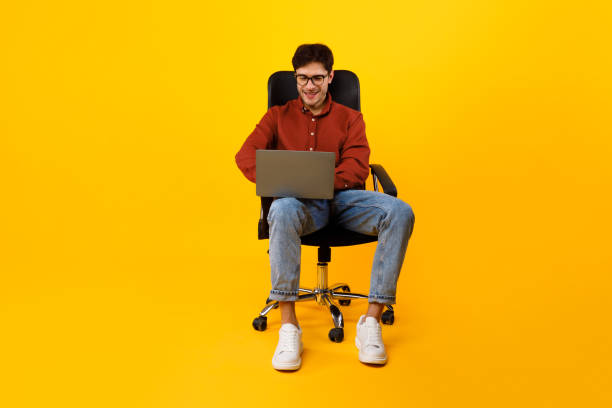 istock Man Using Laptop Computer Sitting In Chair Over Yellow Background 1480361140