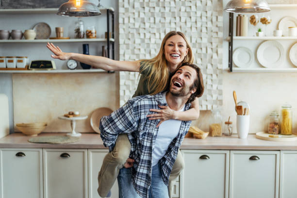 happy young european guy rolls his wife on back and have fun together in modern kitchen interior in own home - domestic kitchen contemporary domestic room lifestyles imagens e fotografias de stock