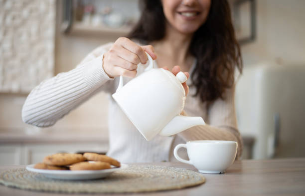 istock Happy young woman pouring herbal tea in mug, sitting at table in kitchen interior, selective focus 1480362889