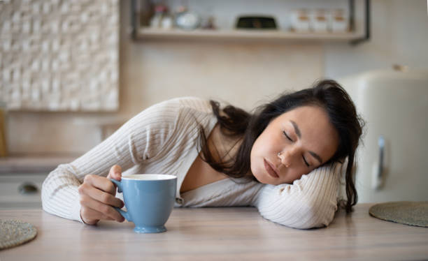 istock Tired woman with coffee cup sleeping on table in modern light kitchen interior, lying on table with closed eyes 1480362913