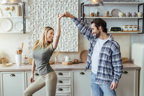 satisfied european millennial man with stubble and blonde lady enjoy free time, have fun and dance - two parent family indoors home interior domestic kitchen imagens e fotografias de stock