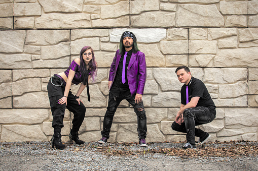 A rock band dressed in black and purple against a stone wall.