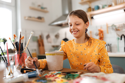 Adorable smiling girl painting flower pot in a domestic room