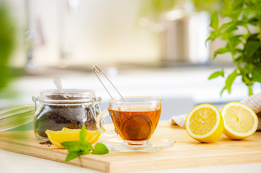 A glass cup with hot tea and a kettle on a bright table by the window. Tray with different varieties of herbal tea on a white background. A delicious and healthy drink to strengthen immunity.