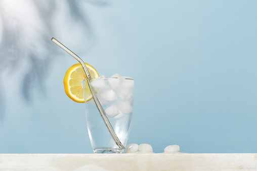 Glass of cold water with ice cubes and lemon slice on the table, sunny composition