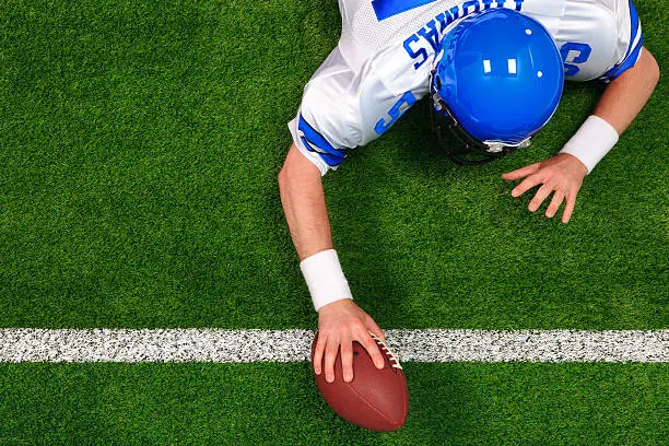 Overhead photo of an American football player making a one handed touchdown. The uniform he's wearing is one I had made using my name and does not represent any actual team colours.
