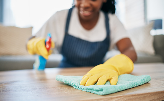 Hand, cloth and gloves with a black woman cleaning a home for hygiene as a housekeeper or maid. Furniture, bacteria and chemical with a female cleaner working in housekeeping in an apartment