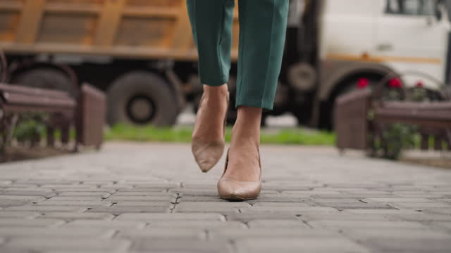 Stylish woman in high heel shoes walks on paving slabs road