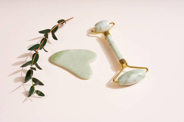 istock Cosmetic background roller for the face, anti-aging scraper guasha eucalyptus leaves. Pastel pink background skin care set. 1480377556