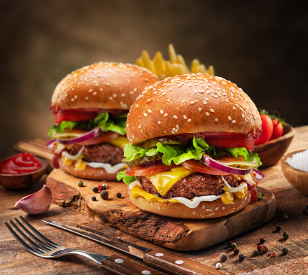 Tasty cheeseburgers or hamburgers and french fries on wooden tray.