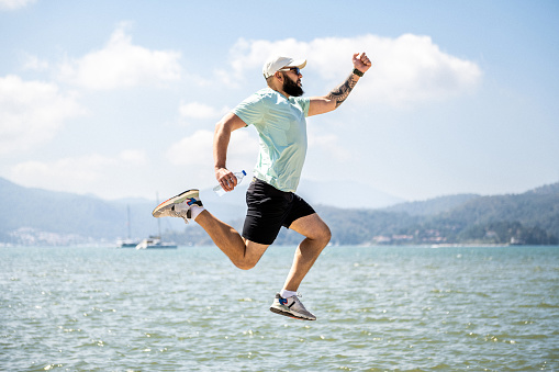 Jumping in to the summer vacations. Happy man jumping and fooling around against beautiful sea and mountains