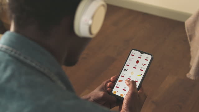 Black Man Using Food Delivery App on Smartphone at Home