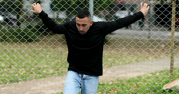 Hispanic guy leaning on metal fence outside. Latino south american person