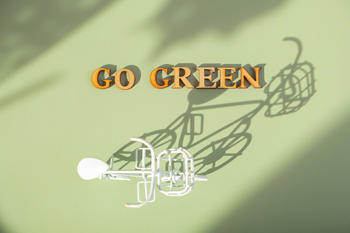Go green text with bycicle on green background with hard shadows. Sustainable lifestyle concept.