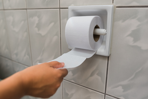woman's hand pulling a roll of toilet paper