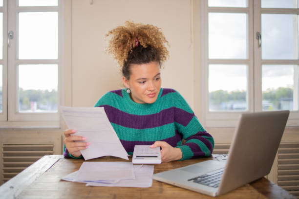Young woman using calculator while going through bills and home finances stock photo