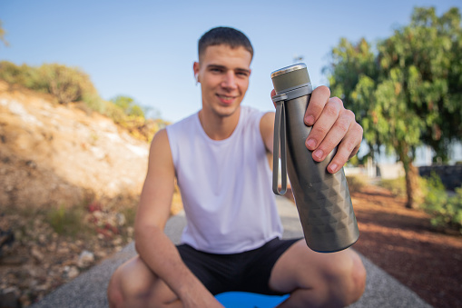 A smiling sportsman is holding a bottle of water while exercising