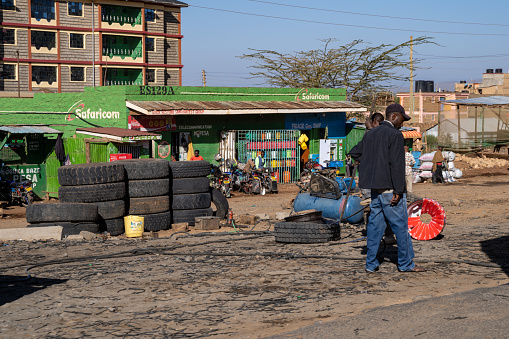 Kenya, East Africa - March 3, 2023: Men work with tires along the roadside in a rural village in Kenya. Safaricom mobile telephone shop in background