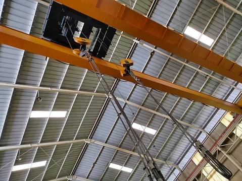 Yellow overhead crane installed on the manufacturing industry plant shop. Jib crab trolley with hooks and linear traverse.
