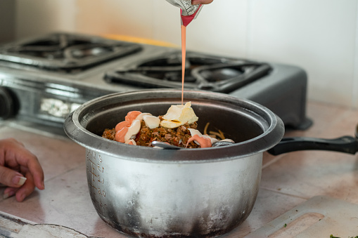 woman pouring pink sauce over the pot with spaghetti