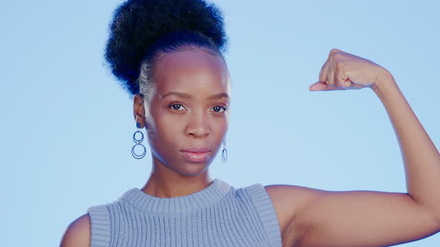 Strong, muscle and face of a black woman with biceps isolated on a blue background in a studio. Serious, confident and portrait of an African girl with power, empowerment and showing gym progress
