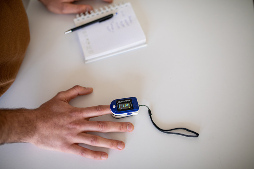 Unrecognizable man measuring oxygen saturation with digital pulse oximeter at home.