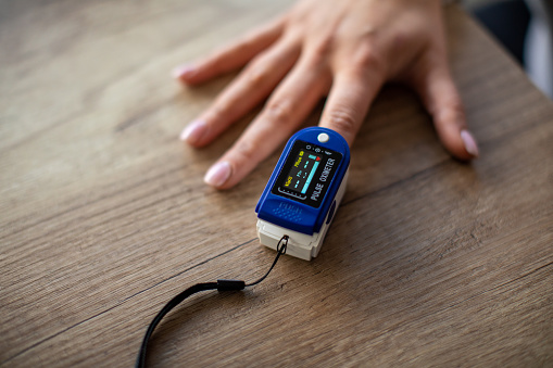 Woman measuring oxygen saturation with digital pulse oximeter at home.