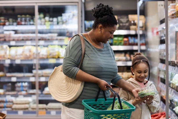 Mother shopping in supermarket with little daughter and buying vegetables