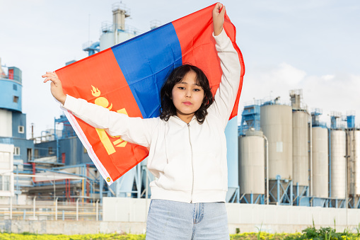 National flag of Mongolia in hands of girl against background of modern factory