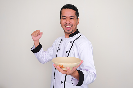 Asian chef clenched fist showing excited expression while holding empty bowl