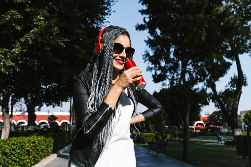Young latin woman with braids hair holding beverage drink soda can on the street in Mexico, hispanic people