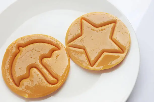 Photo of Dalgona candy or Ppopgi. Sugar Honeycomb cookie with round umbrella and star shape on white plate. candy challenge