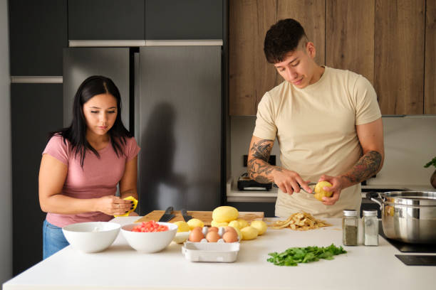 istock Two young latin people peeling potatoes and cleaning kitchen counter at kitchen. 1480469256