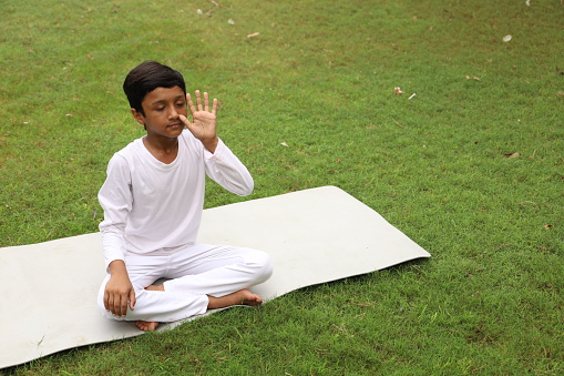 Happy Indian Boy doing Yoga and meditating, exercising with focus and concentration early morning while sitting on a Yoga mat.
