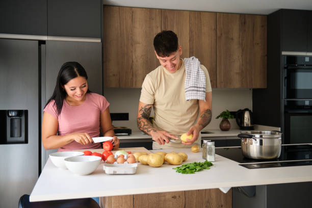 istock Two young latin people peeling potatoes and cutting tomatoes at kitchen. 1480471208