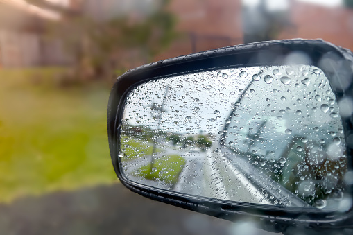 Side view of a car side mirror from inside on car with rain droplet and splashing on the glass window background. Weather Concepts.