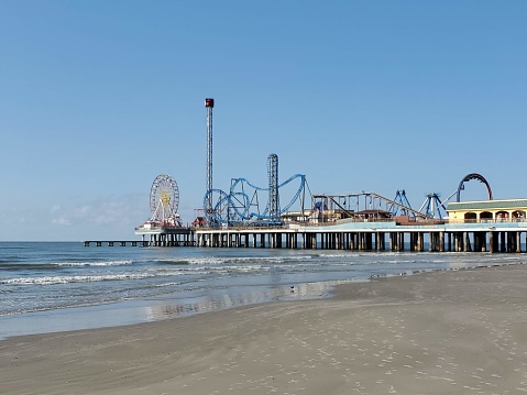 Wide Shot of Galveston Beach and Pier with waves rolling into the sandy beach.