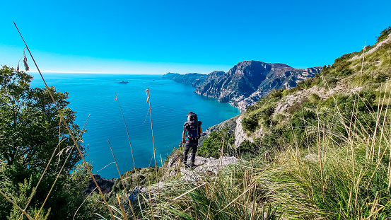 Man with panoramic view from hiking trail Path of Gods between coastal towns Positano and Praiano. Trekking in Lattari Mountains, Apennines, Amalfi Coast, Campania, Italy, Europe. Mediterranean Sea