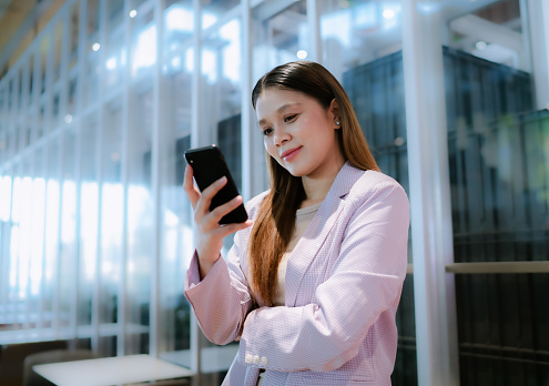 A young Asian woman communicating with her client through her smartphone.