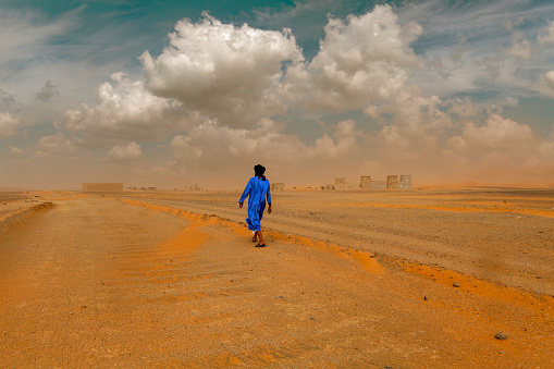 A Tuarek dressed in traditional blue clothes walks along the road in Merzok, Morocco. Merzouga region