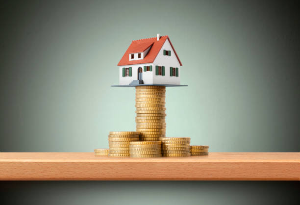 Miniature model house standing on a stack of coins stock photo