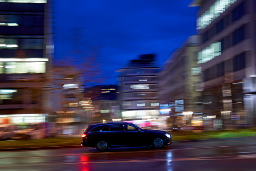 Stuttgart, Germany - February 03. 2023: Sports sedan on slippery road at night in motion. Car in the rainy city. Panning shot.