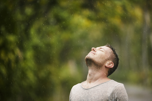 Portrait of man in wet clothes with eyes closed enjoying heavy rain in nature. Themes of life water, weather and environment.