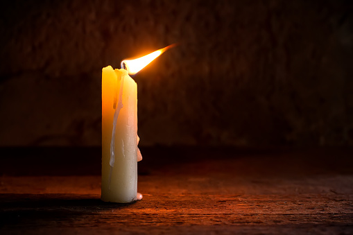 A lit candle in the breeze. A candle in the twilight. The flame of the candle fluctuates under the breeze.