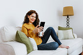latin adult woman using phone and resting on sofa at home in Mexico, Hispanic female lifestyles